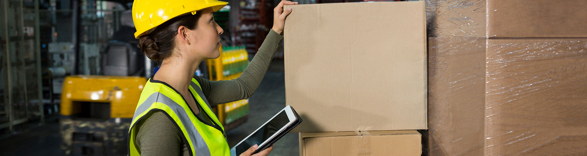 mulher com tablet na mão em frente a uma pilha de caixas de carga ensinando como calcular o valor do seguro de carga